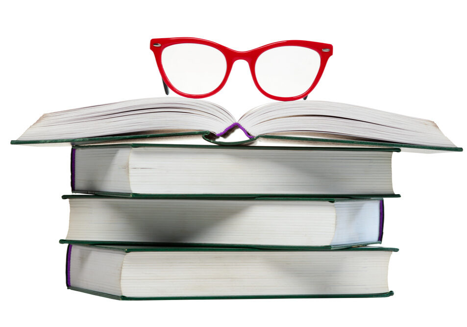 red glasses on open book, pile or stack of books isolated over white background